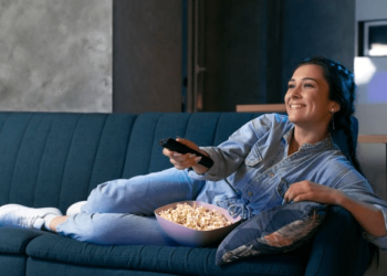 mulher sentada sofá controle remoto televisão assistindo tv sorrindo cliente feliz assinante tv paga