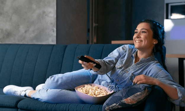 mulher sentada sofá controle remoto televisão assistindo tv sorrindo cliente feliz assinante tv paga