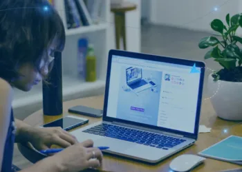 Mulher de cabelos curtos segurando lápis mão direta na frente um notebook ligado objetos sobre a mesa